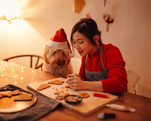 Perro con gorro de Papá Noel horneando galletas con una mujer con delantal