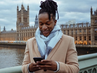 A person standing in front of England’s Palace of Westminster while checking phone.