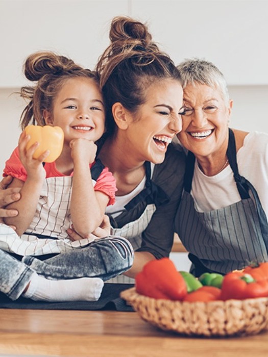 Three generations of women laughing together in a kitchen.