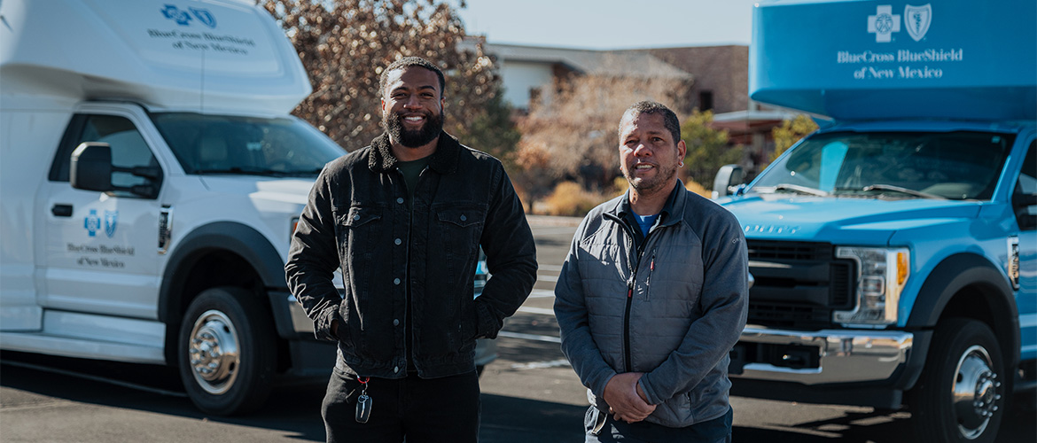 Two men stand in front of two mobile care vans